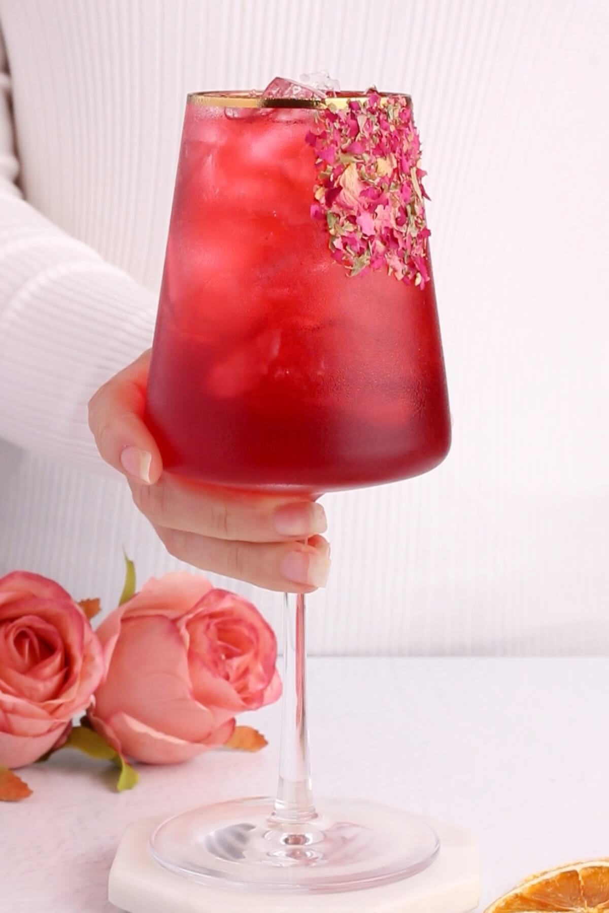 hibiscus mocktail recipe is a wine glass with a gold rim garnished with a rose petal rim.