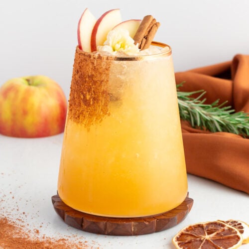 apple cider mocktail in a short tumbler with a gold rim garnished with apple slices and cinnamon.
