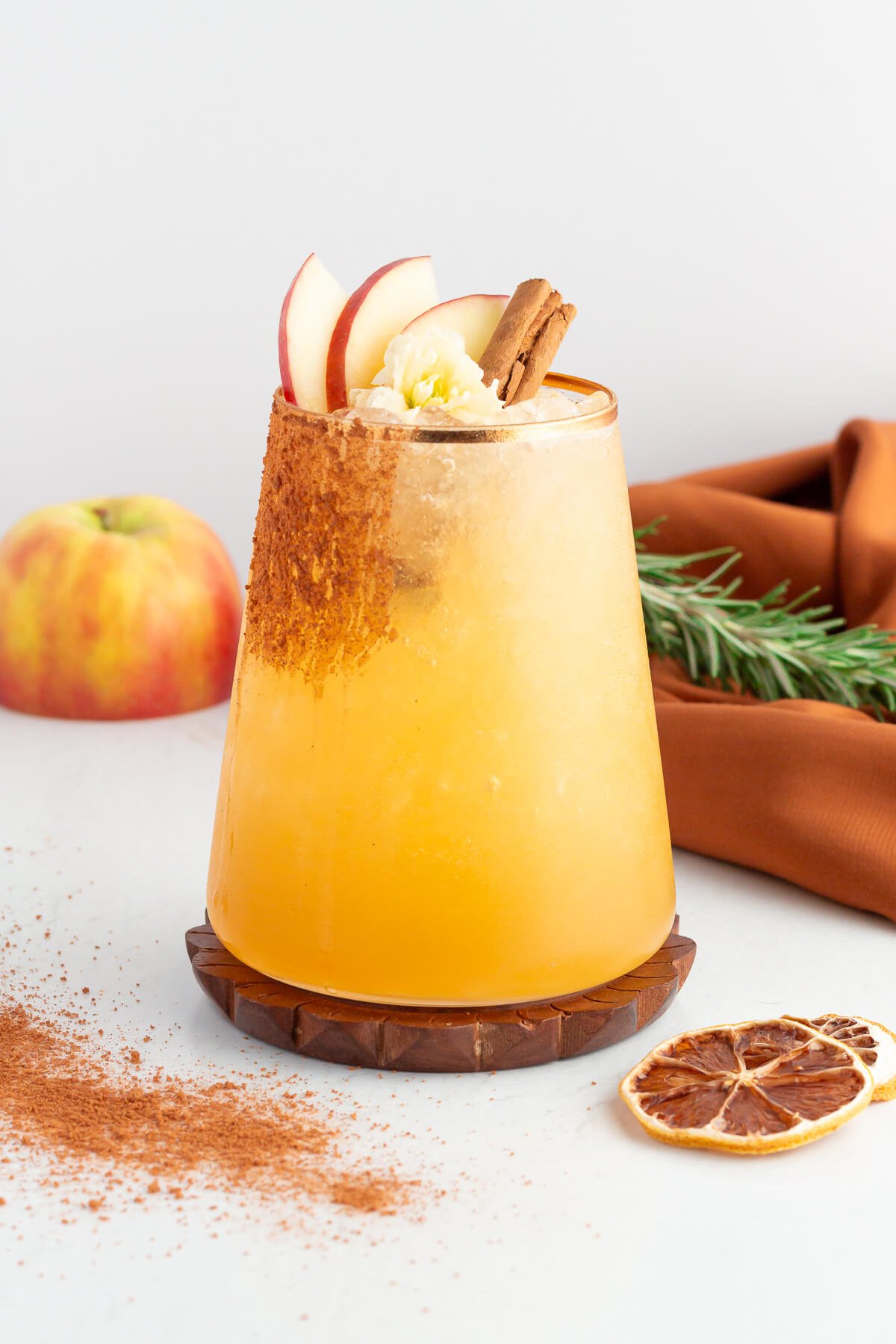 apple cider mocktail in a short tumbler with a gold rim garnished with apple slices and cinnamon.