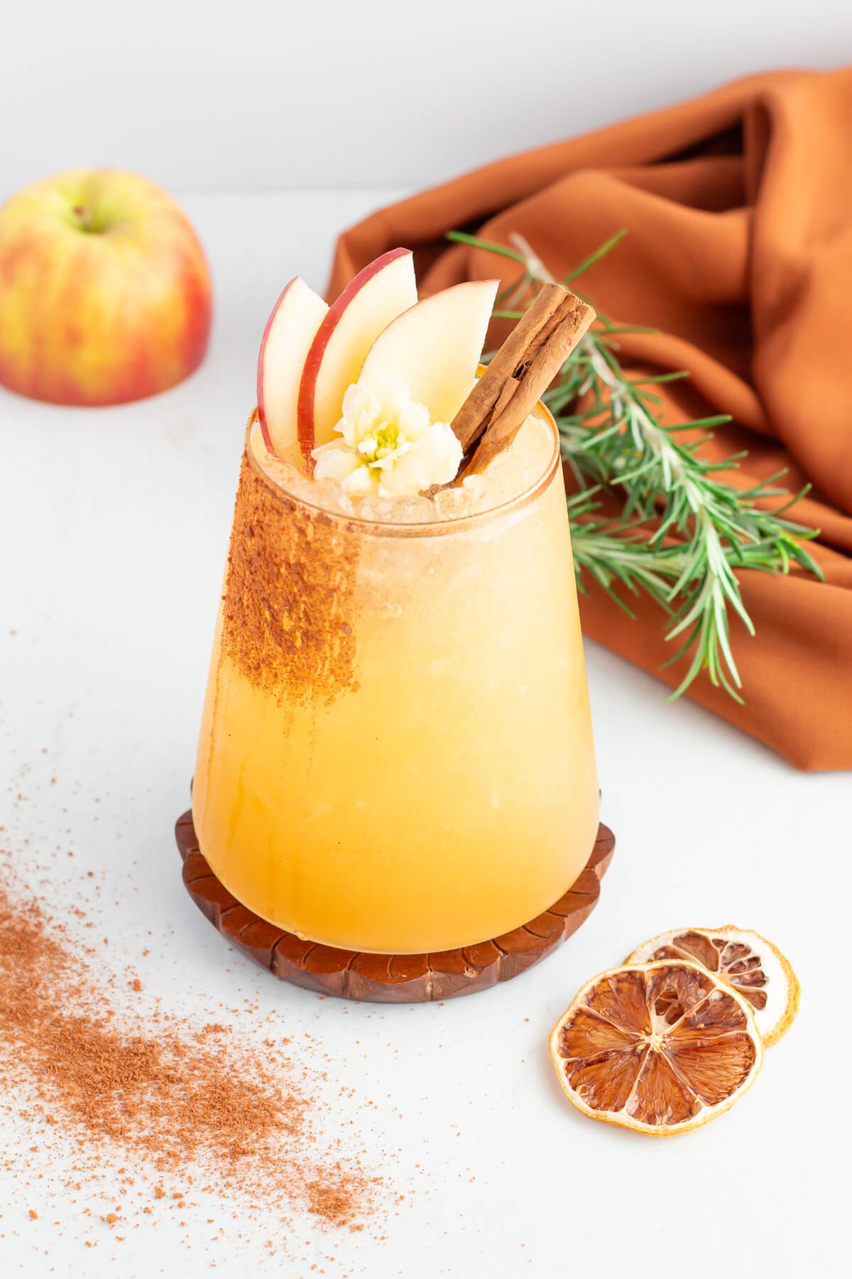 image looking down at apple mocktail in tumbler with dehydrated citrus, rosemary and cinnamon scattered around the base.