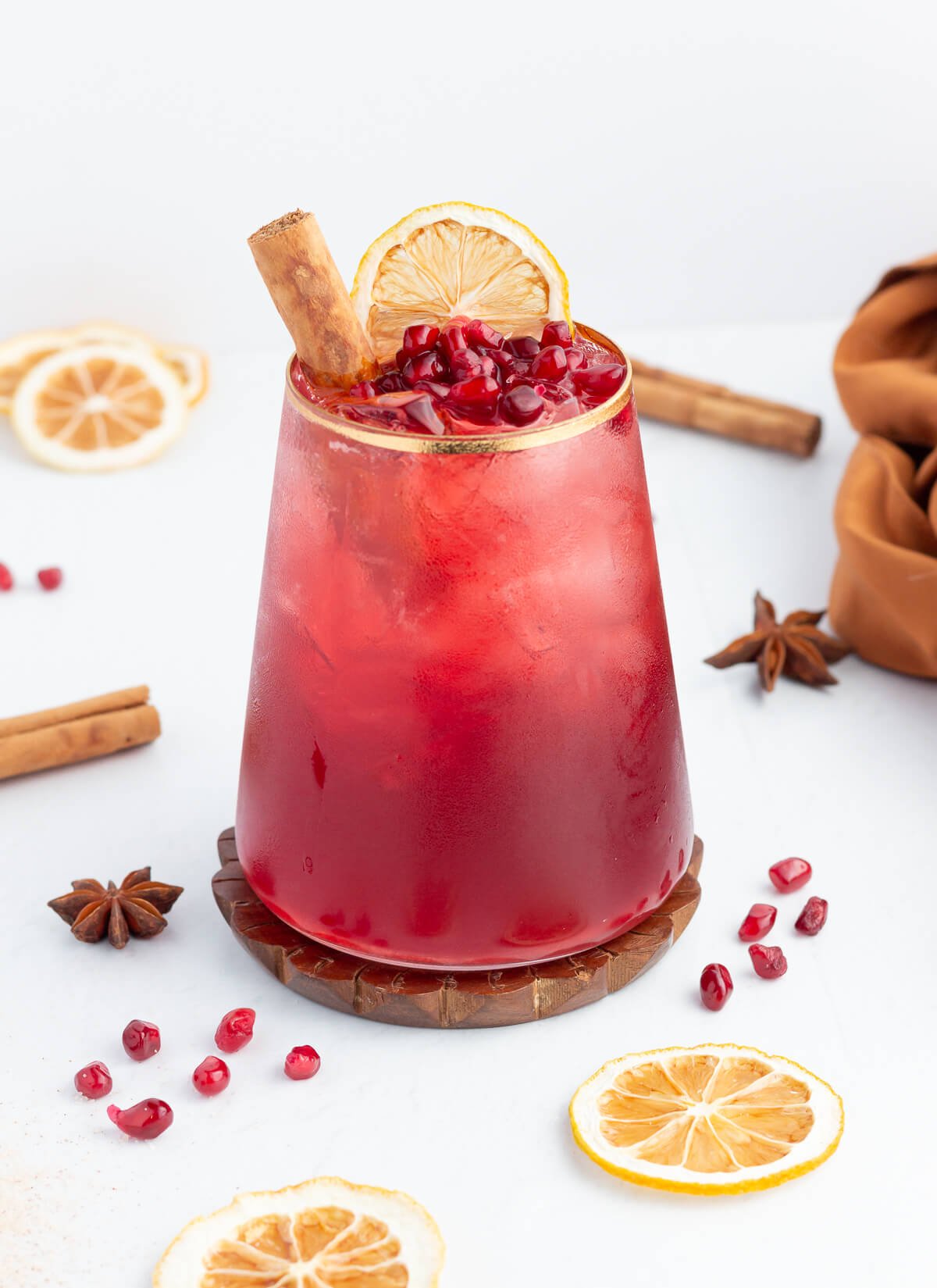 cinnamon mocktail in a short glass with a gold rim garnished with cinnamon pomegranate and orange