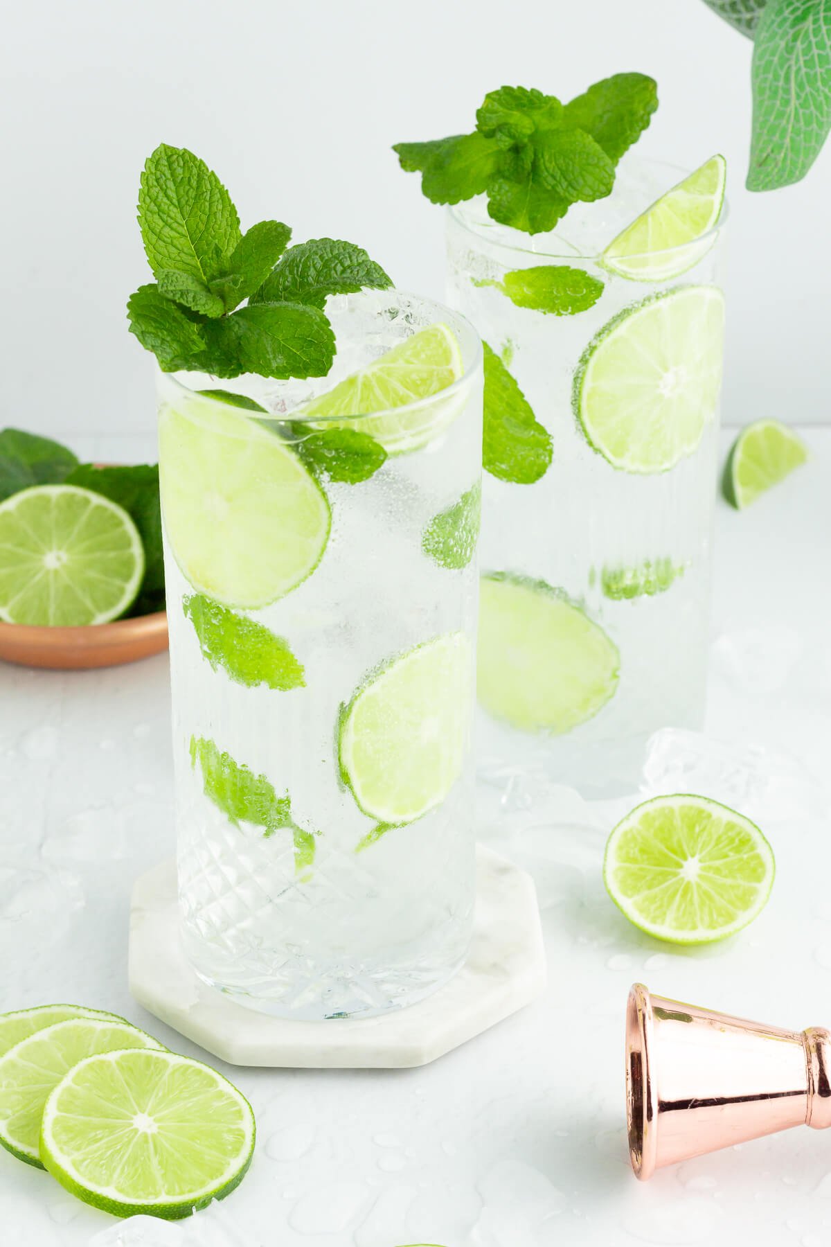 two mojito mocktails with mint and lime in tall glasses on a white background.