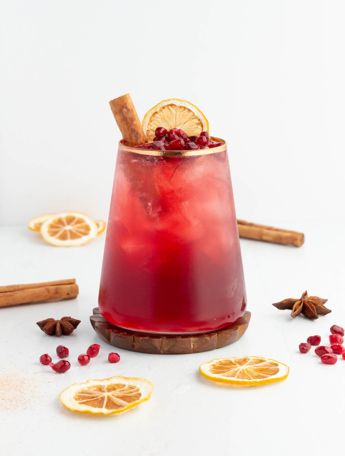 red mocktail in a short tumbler garnished with pomegranate orange and cinnamon