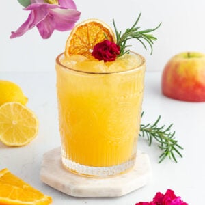 mocktail made with rosemary orange and apple and garnish with fresh rosemary and an edible flower.