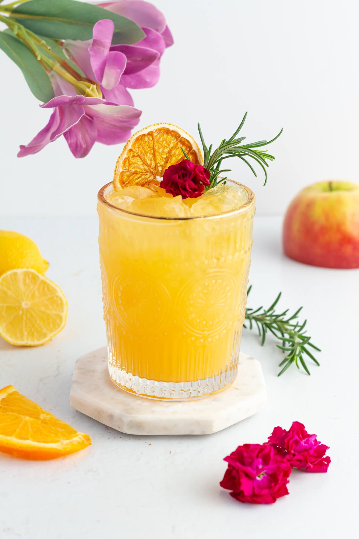 mocktail made with rosemary orange and apple and garnish with fresh rosemary and an edible flower.