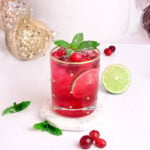 red mocktail for the holiday in a gold rimmed glass garnished with cranberry and mint.