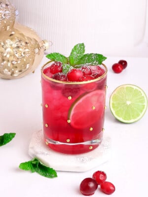 red mocktail for the holiday in a gold rimmed glass garnished with cranberry and mint.