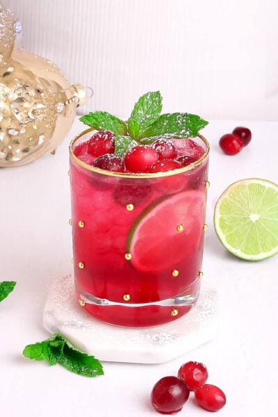 red mocktail for the holiday in a gold rimmed glass garnished with cranberry and mint.