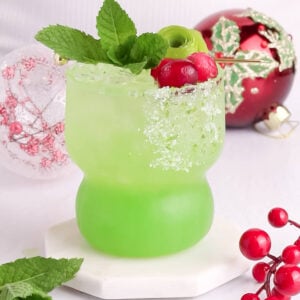 bright green mocktail in a short glass with red garnishes on a white background.