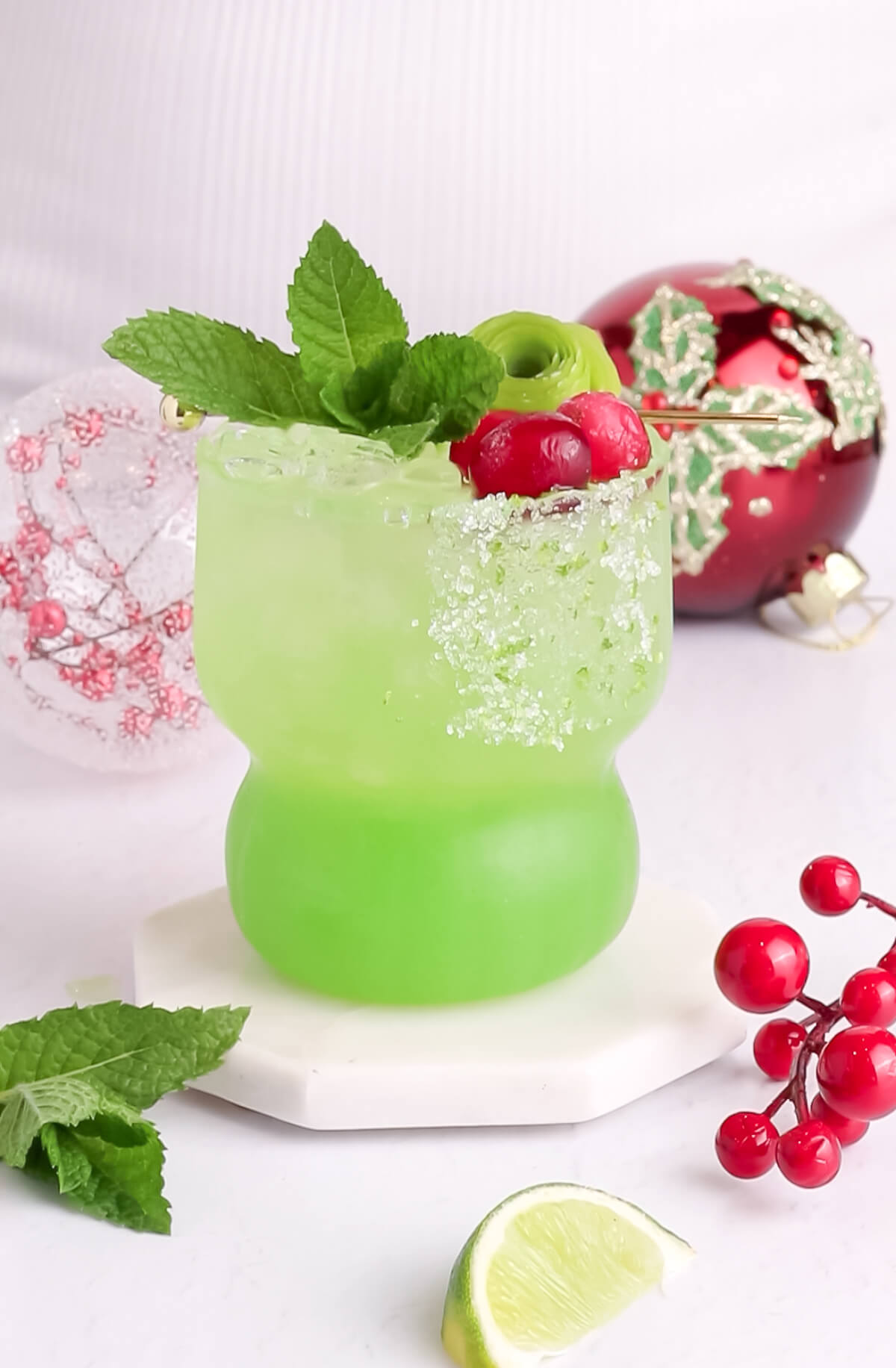 bright green mocktail in a short glass with red garnishes on a white background.