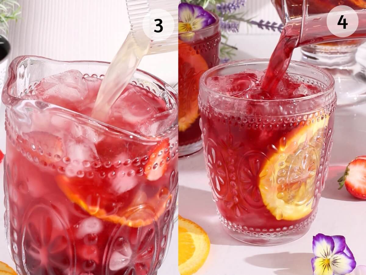 A close-up of a decorative glass filled with ice, orange and strawberry slices, as sparkling hibiscus sangria is poured in. Another glass with the same sangria is being poured beside it, surrounded by fruit and edible flowers.