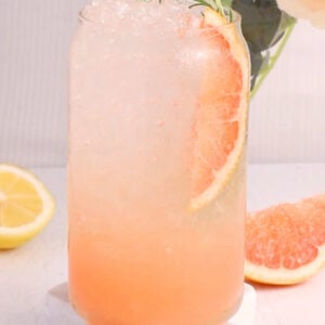 A glass featuring a refreshing grapefruit mocktail, topped with a slice of grapefruit and a sprig of rosemary.
