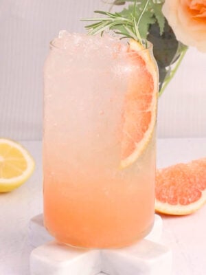 A glass featuring a refreshing grapefruit mocktail, topped with a slice of grapefruit and a sprig of rosemary.