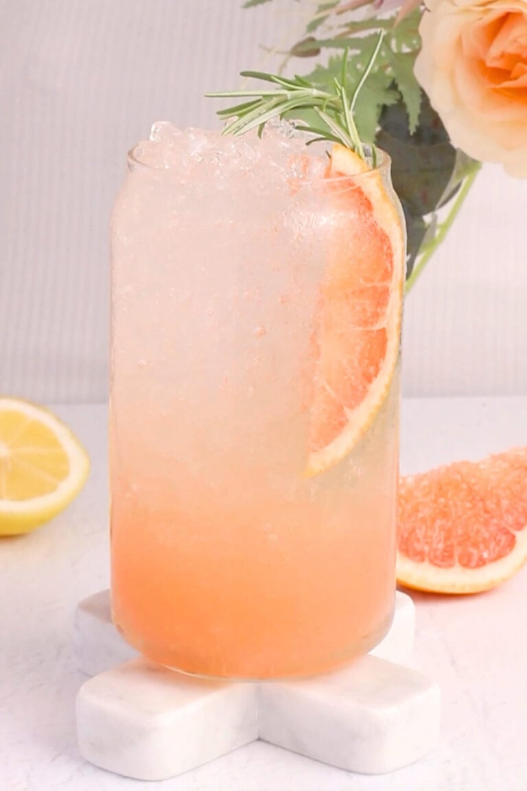 A glass featuring a refreshing grapefruit mocktail, topped with a slice of grapefruit and a sprig of rosemary.
