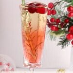 A festive glass of mocktail garnished with cranberries and a rosemary sprig is set beside holiday decorations with red berries. Text at the bottom reads Christmas Morning Mocktails.