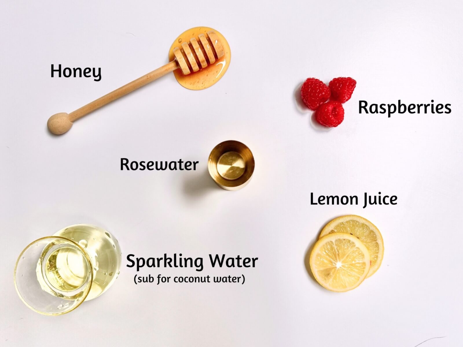A flat lay of honey with a dipper, three raspberries, a small cup of rosewater, three lemon slices labeled lemon juice, and a glass of sparkling water with text labels for each ingredient.