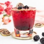 A blackberry mocktail in a gold-rimmed glass, garnished with fresh blackberries and a dehydrated citrus slice.