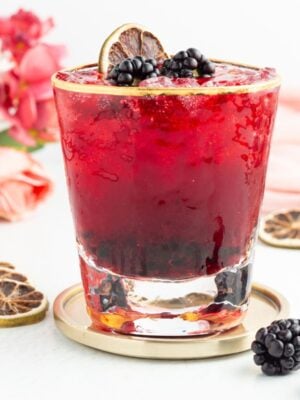 A blackberry mocktail in a gold-rimmed glass, garnished with fresh blackberries and a dehydrated citrus slice.