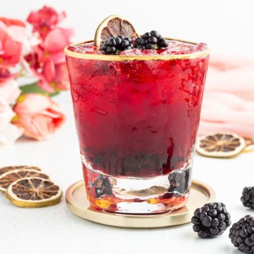 A blackberry mocktail in a gold-rimmed glass, garnished with fresh blackberries and a dehydrated citrus slice.