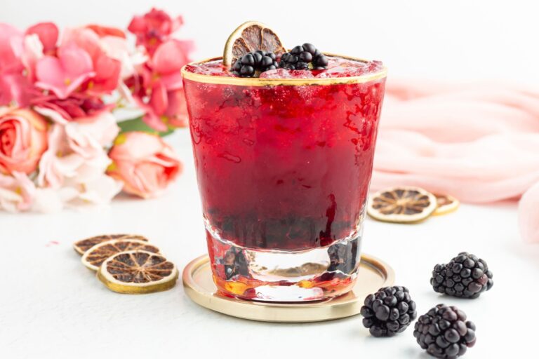 A blackberry mocktail in a gold-rimmed glass, garnished with fresh blackberries and a dehydrated citrus slice.